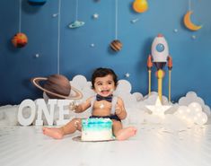 a baby sitting on the floor with a cake in front of him and space themed backdrop