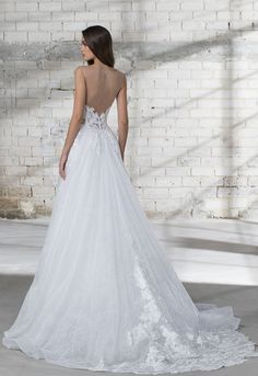 a woman in a white wedding dress standing against a brick wall with her back to the camera