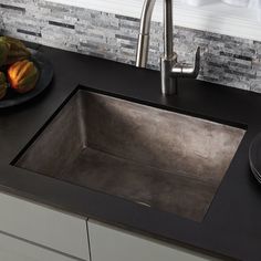 a kitchen sink sitting under a faucet next to a bowl of fruit