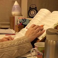 a woman sitting at a desk with an open book and coffee mug in front of her