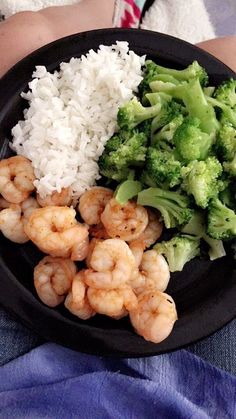 shrimp, rice and broccoli on a black plate in someone's lap