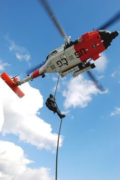 a man hanging from the side of a helicopter while being hoisted by a person with a rope