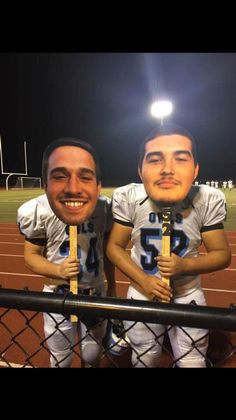 two football players are holding up their trophies on the sidelines at night with stadium lights in the background