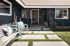 a bench sitting in front of a house next to a grass covered yard with potted plants