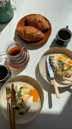 two plates with eggs and croissants on them next to cups of coffee