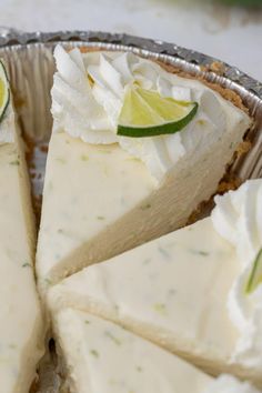 a pie with limes and whipped cream on top sits in a tin foil pan