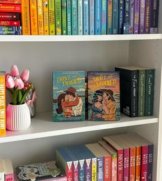 several books on a white book shelf with pink tulips