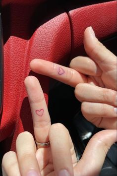 two fingers with hearts drawn on them are touching each other's fingers in front of a car steering wheel