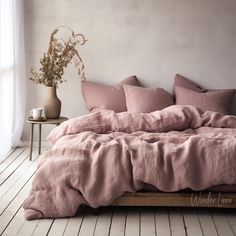 an unmade bed with pink linens in a white room next to a window