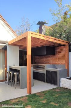 an outdoor kitchen and bar area in a back yard with wooden pergolan roof