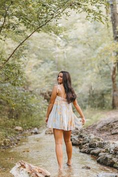 a woman in a white dress is walking through the water on a rocky path near some trees