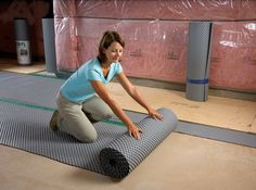 a woman kneeling down on the floor with a roll of insulation