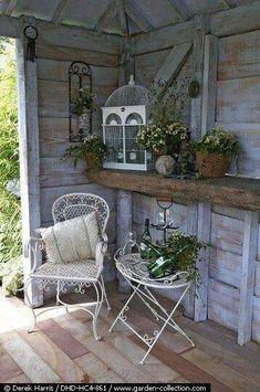 an outdoor patio with two chairs and a birdcage on the wall, surrounded by potted plants