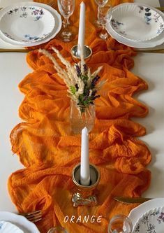 the table is set with orange linens and place settings