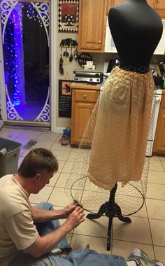 a man sitting on the floor working on a mannequin's dress form