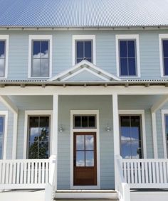 a blue house with white railings and steps leading up to the front door on a sunny day