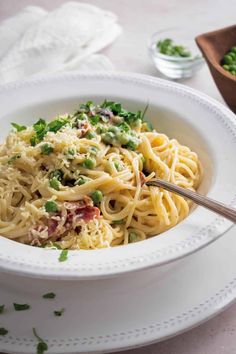 a white bowl filled with pasta and garnished with parsley on the side