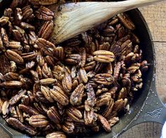 pecans are being cooked in a skillet with a wooden spoon on the side