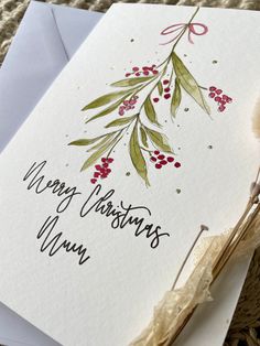 a christmas card with red berries and green leaves on it, sitting on top of a piece of paper