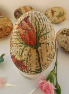 an egg decorated with flowers and leaves on top of a white surface next to pink flowers