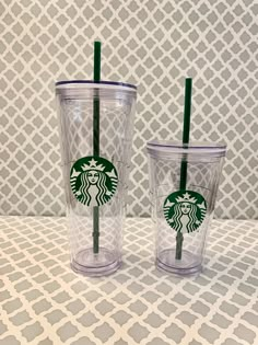 two starbucks cups with green straws sitting on top of a white and gray table