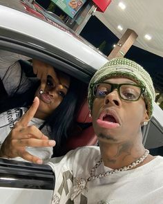 two people sitting in a car with one pointing at the camera and the other looking surprised