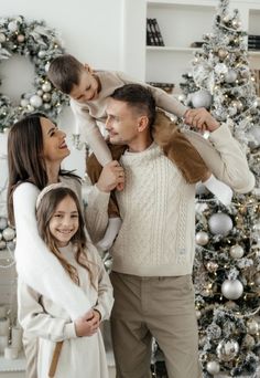 a man and woman are standing in front of a christmas tree with their son on his shoulders