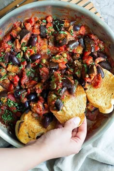 a person is holding bread with black olives and tomato sauce in a skillet