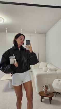 a woman taking a selfie in her living room while holding a coffee cup and cell phone