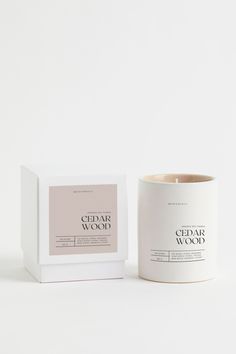 a candle that is next to a box on a white surface with the words cedar wood printed on it