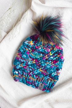 a knitted beanie with multicolored yarn and a pom - pom