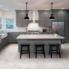 a kitchen with gray cabinets and marble counter tops, two stools in front of the island