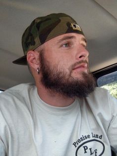 a man with a beard wearing a camo hat in the back seat of a car