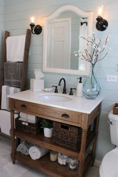 a white toilet sitting next to a bathroom sink under a mirror and a wooden shelf