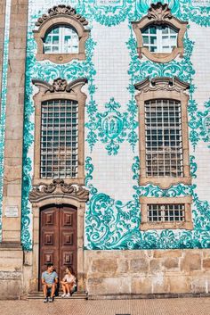 two people sitting on the steps in front of a building with blue and white tiles