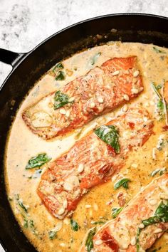 some fish is cooking in a skillet on the stove top with spinach and tomatoes