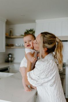 a woman holding a baby up to her face while standing on a counter in a kitchen