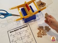 a child's hand holding a pair of scissors next to cookie cutters on a table