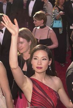 a woman in a red dress waves to the crowd as she walks down the red carpet