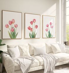 three pink tulips are hanging on the wall next to a white couch in a living room