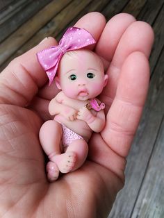 a hand holding a tiny baby doll with a pink bow on it's head