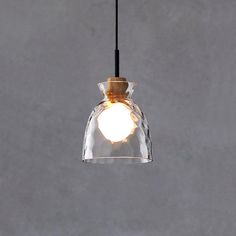 a clear glass light hanging from a black cord on a gray wall with a white ball in the center