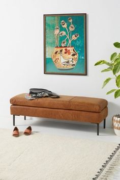 a brown bench sitting in front of a painting on the wall next to a plant