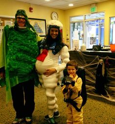 two people in costumes standing next to each other with a child holding a camera and smiling at the camera