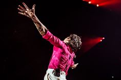 a man in pink shirt and white pants on stage with his arms out to the side