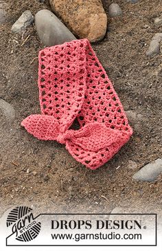 a pink crocheted scarf laying on the ground next to some rocks and stones