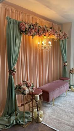 a room decorated in pink and green with flowers on the wall, chandelier and bench