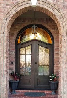 an arched door with two potted plants on the front step and glass windows above it