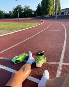 someone's feet resting on the edge of a running track with their green shoes