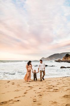 a man and woman holding hands while walking on the beach with a small child in front of them